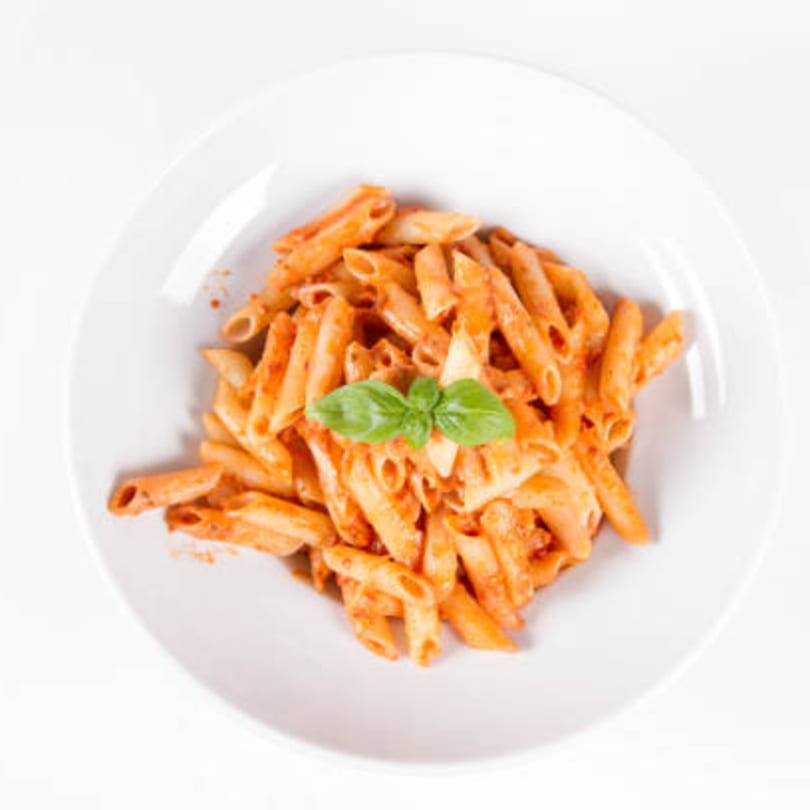 Penne pasta with red sauce and a fresh basil garnish in a white bowl.