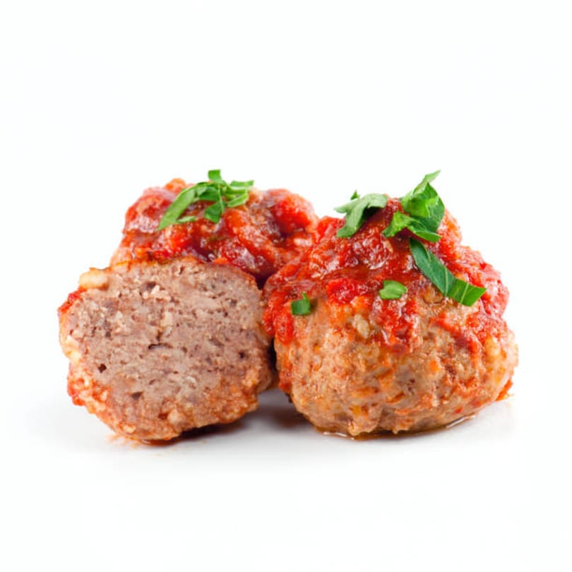 Two By the Bucket Italian meatballs, one sliced open, topped with red sauce and green herbs.
