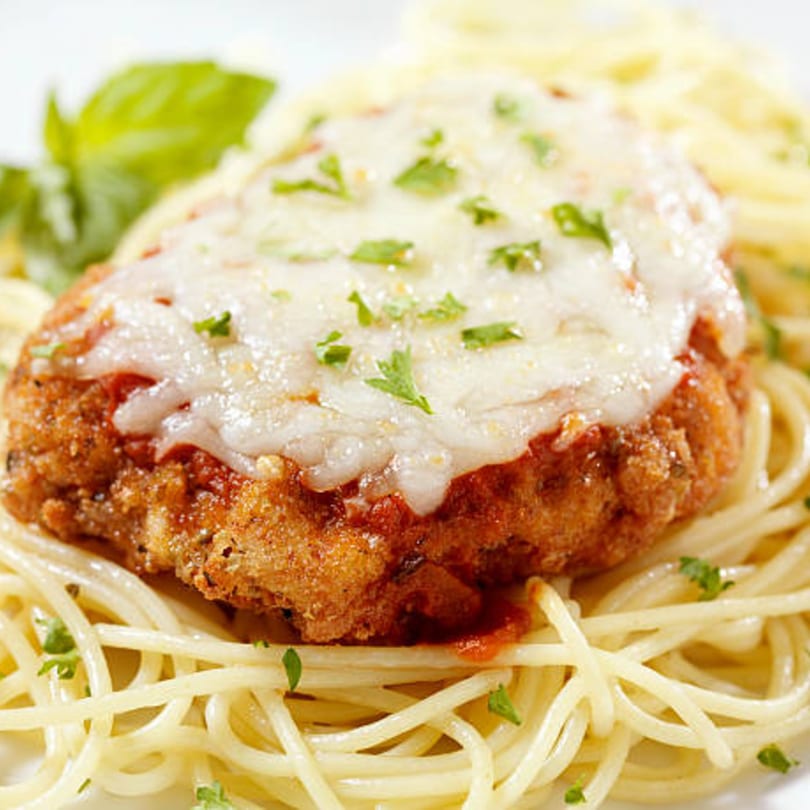 Chicken Parmesan with melted cheese and parsley, served over spaghetti with a basil garnish.