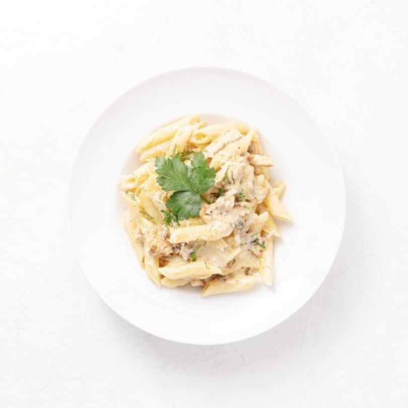 Creamy penne pasta with chicken and parsley on a white plate from By the Bucket.
