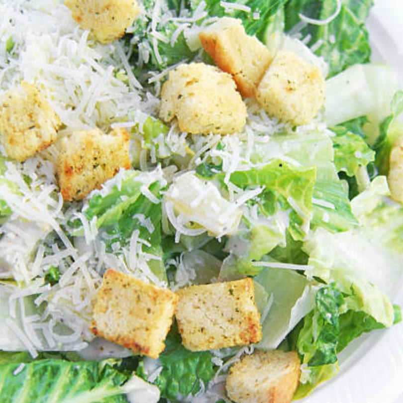 Close-up of a Caesar salad with crisp romaine lettuce, creamy dressing, croutons, and shredded Parmesan.
