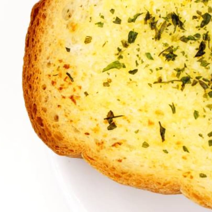Close-up of a golden-brown slice of garlic bread topped with green herbs.